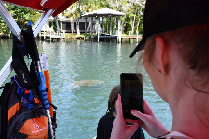 Person on boat takes photo of water, gear in background.