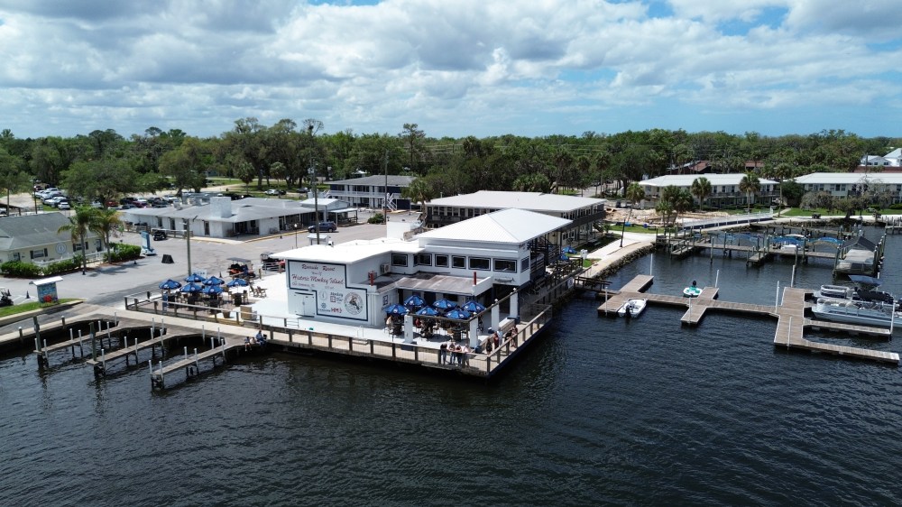 Waterfront restaurant with outdoor seating, boat docks, and cloudy sky.