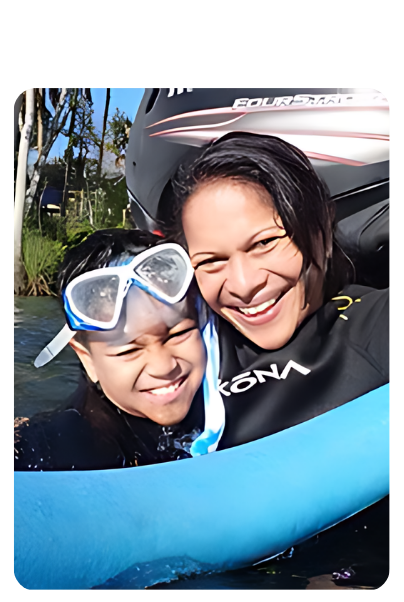 Two people smiling in wetsuits, one wearing snorkeling gear, near water.