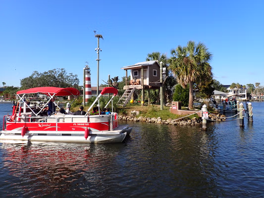 Red boat near small monkey island with a hut and palm trees on a sunny day.