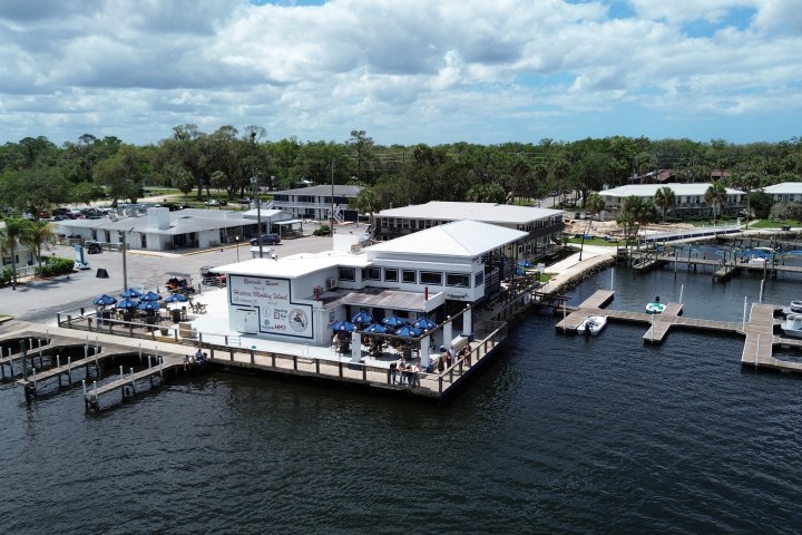 Waterfront restaurant with outdoor seating and docks, surrounded by trees.